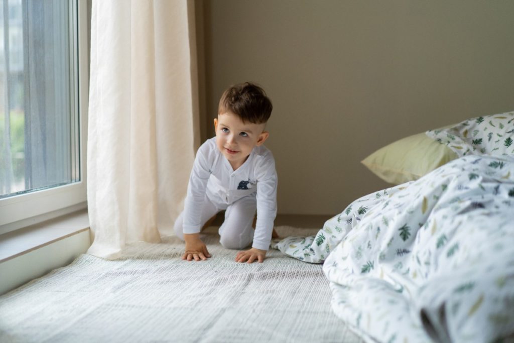 un petit garçon est à 4 pattes dans une chambre sur un tapis. il est en pyjama.