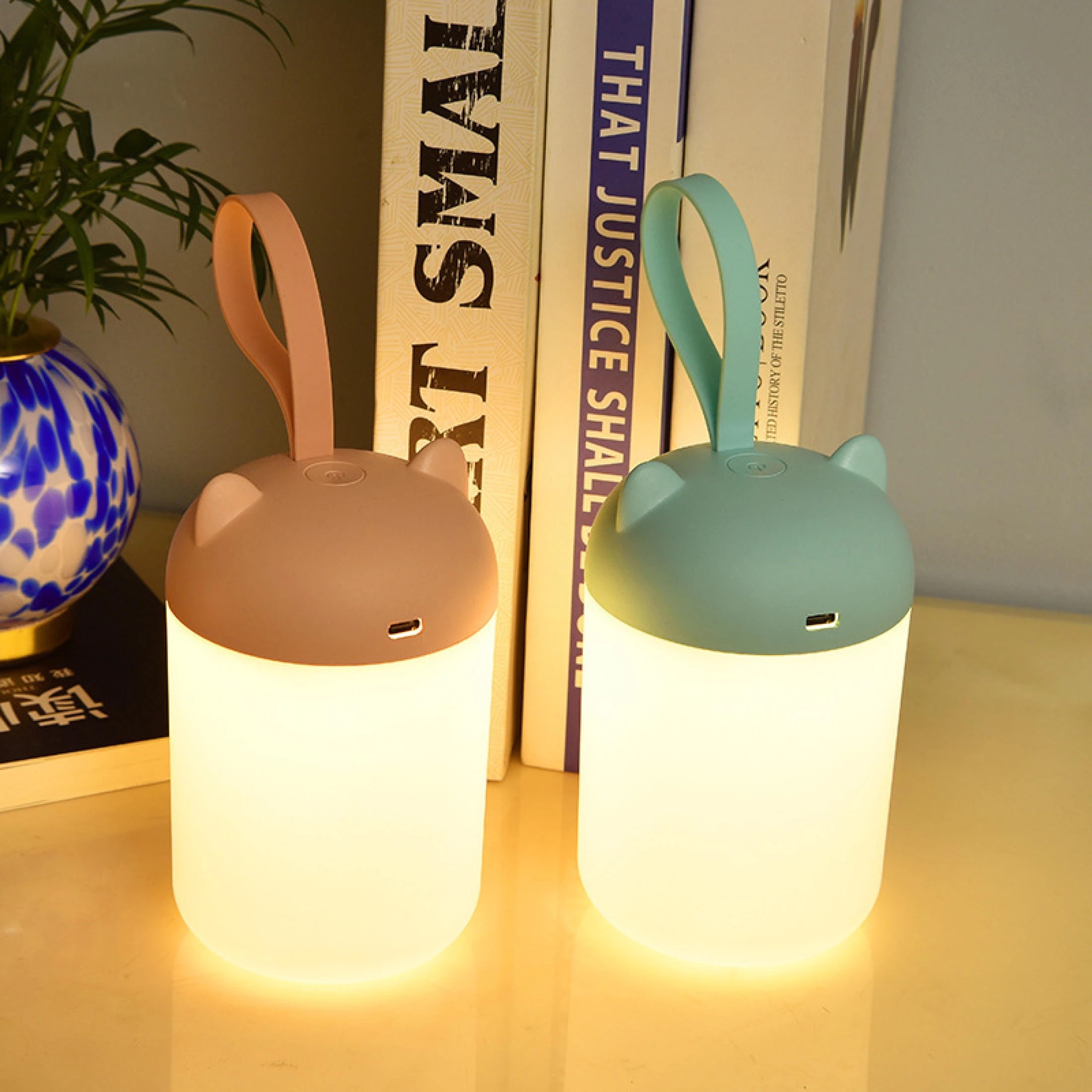 Veilleuse tactile LED portable et rechargeable par USB. Bonne qualité et à la mode avec deux couleurs disponibles au-dessus d'une table avec des livres à cotés dans une maison.