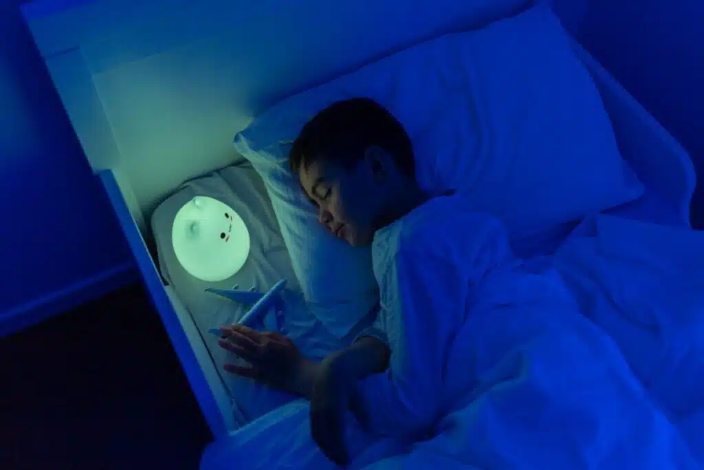 un enfant dot dans sa chambre dans son lit. il a une main posée sur un avion. une veilleuse est allumée près de son visage sur son lit.