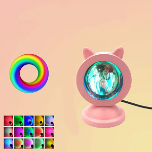 Sur fond rose, une veilleuse projection ronde dont la coque est rose avec ndes petites oreilles de chats et un petit socle, sur le coin inférieur gauche plusieurs petites images déclinent les couleurs possibles, et au dessus un rond rond multicolore suggère le panel de couleurs possible avec cet outils