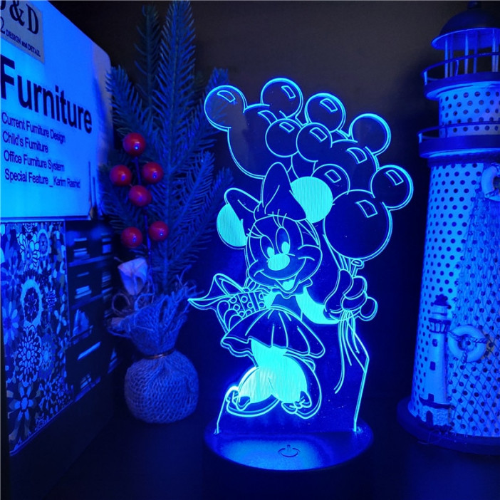 Veilleuse de Minnie avec un cadeau sous un bras et des ballons dans l'autre en tête de mickey dans l'autre , la lumière est bleue, la lampe se trouve sur un bureau avec des bibelots à droite et des livres à gauche