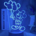 Veilleuse de mickey en train de tenir deux ballons gonflés dans sa main droite , la lumière est bleue, la lampe se trouve sur un bureau avec des bibelots à droite et des livres à gauche