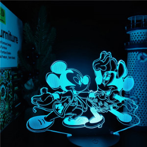 Veilleuse de mickey et minnie en train de danser , la lumière est bleue, la lampe se trouve sur un bureau avec des bibelots à droite et des livres à gauche