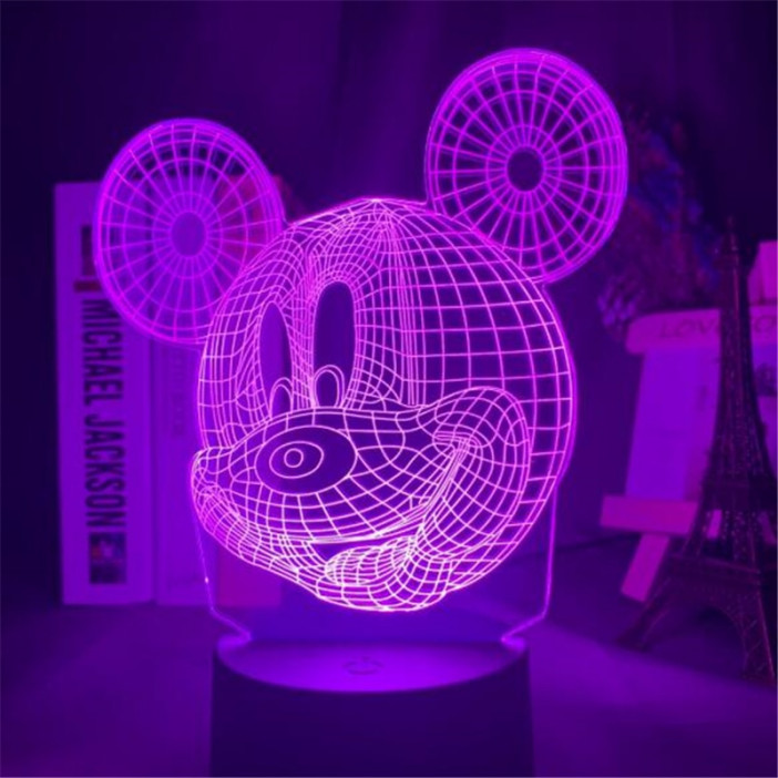 Veilleuse tête de mickey en 3D, la lumière est rose, la lampe se trouve sur un bureau avec des bibelots à droite et des livres à gauche
