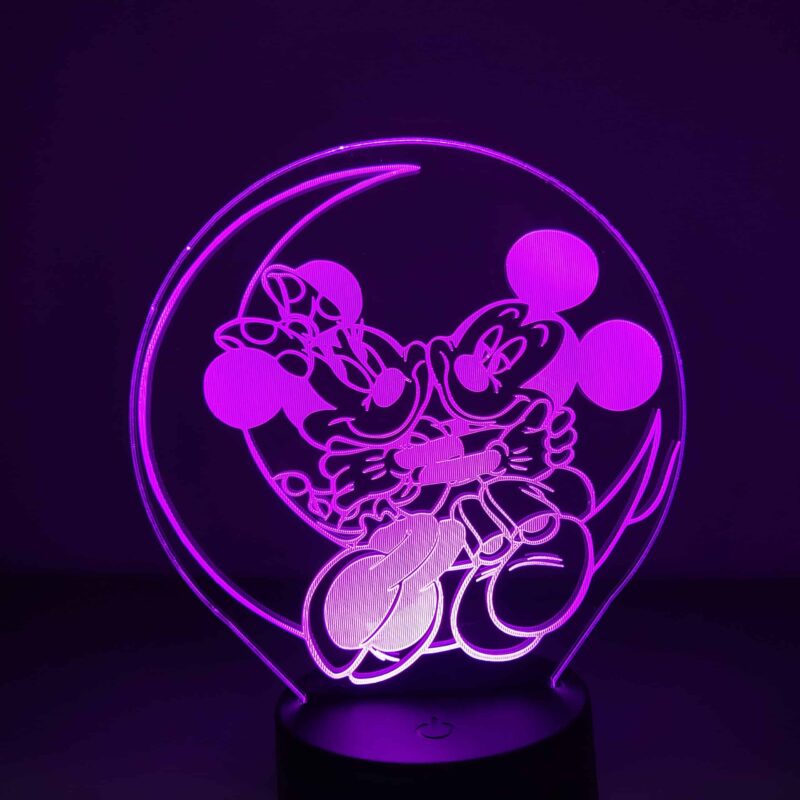 Veilleuse de mickeyet Minnie allongés dans un croissant de lune, la lumière est violette, la lampe se trouve sur un bureau avec des bibelots à droite et des livres à gauche