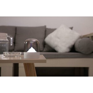 Veilleuse de en forme de montagne blanche posé une table en bois et devant un canapé gris