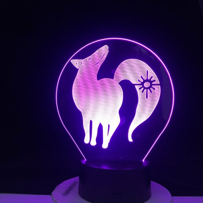 Une veilleuse ronde avec un dessin de renard à l'intérieur de couleur violette sur un socle noir. Sur fond noir.