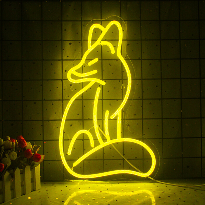 Une veilleuse néon en forme de renard jaune fixé sur un mur de carrelage blanc, en bas à gauche il y a un pot de fleur, dessous une table.