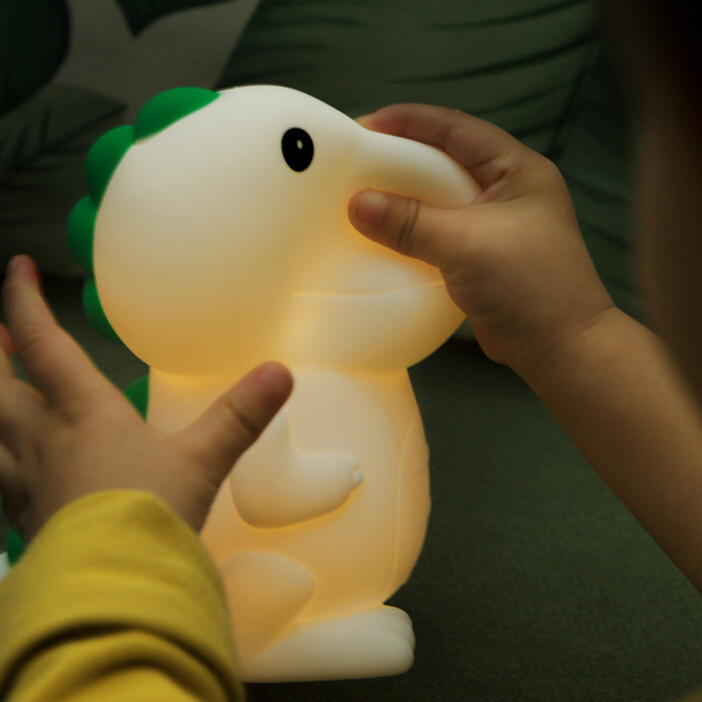 Veilleuse en forme de dinosaure sur laquelle on voit des mains d'enfants en train d'appuyer dessus