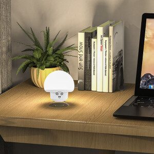 sur un meuble en bois devant une petite plante verte, de livres et un ordinateur portable, une lampe Led veuilleuse en forme de petit champignon est allumé en couleur blanche