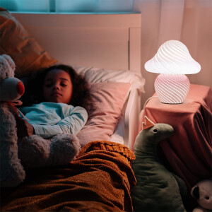 une enfant est installée dans son lit et près d'elle sur un chevet, une lampe Led Veilleuse en forme de champignon blanc est allumée