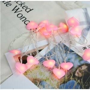 Guirlande lumineuse enfant à motifs de cœurs roses, disposée sur des magazines et photos