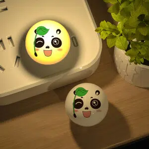 Veilleuse prise en forme de panda à LED, à lumière chaude posé sur un un bureau à côté d'une plante