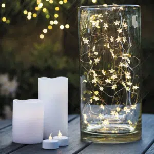 Veilleuse étoile en guirlande LED à piles dans un vase en verre posé près de deux bougies blanches